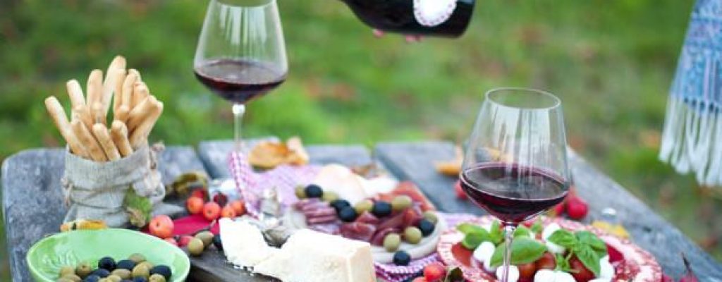 Italian picnic with red wine, parmesan, ham and olives. Lunch in the open air. Traditional snacks. A man pours a glass of wine. Copy space,